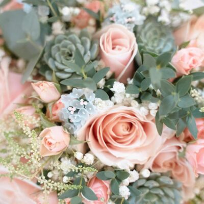 A closeup of a pastel pink rose and succulent bridal bouquet with eucalyptus and white flowers.