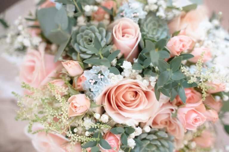 A closeup of a pastel pink rose and succulent bridal bouquet with eucalyptus and white flowers.